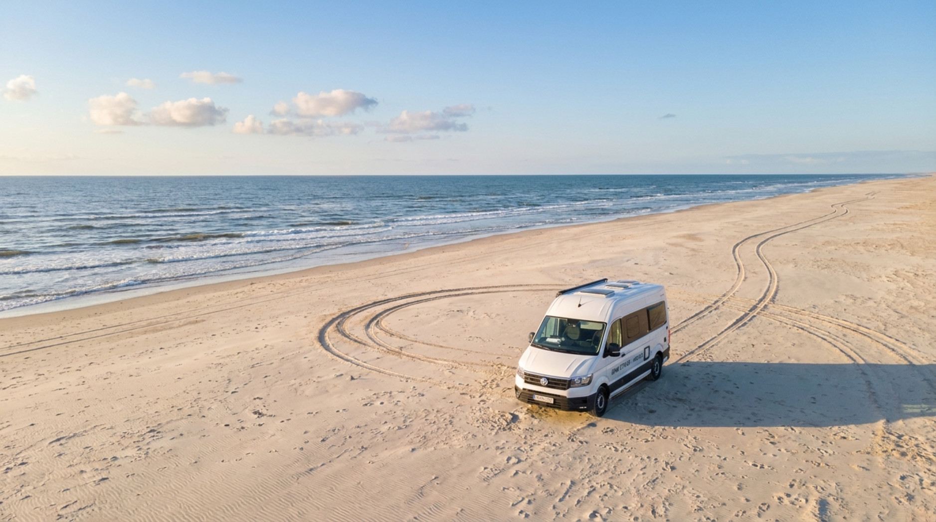 Ein Wohnmobil auf dem Sandstrand von Rømø mit Meereswellen im Hintergrund und Spuren im Sand